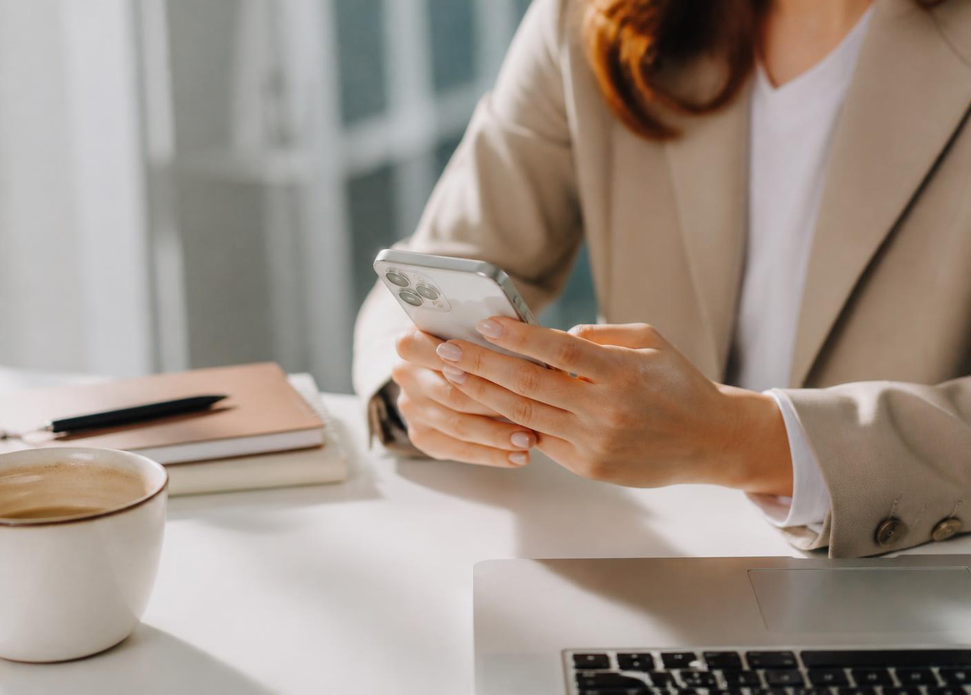 REALTOR reviewing messages on a phone at a bright desk